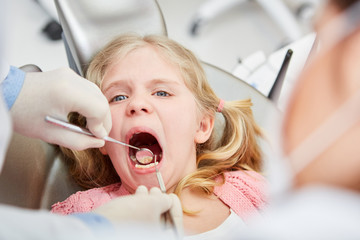 Zahnarzt mit Spiegel untersucht Zähne von Mädchen