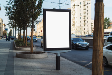 Digital billboard with blank screen for commercial advertising standing in busy street. Road with busy traffic, cars and public transport passing by. People walking along sidewalks, business buildings