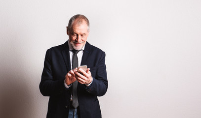 Portrait of a senior man with smartphone in a studio, text messaging.
