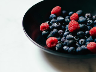 Blueberries and Raspberries in a black dish on a white marble background