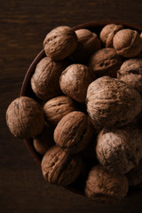  Walnuts nuts in a bowl on a dark brown wooden background in a dark key