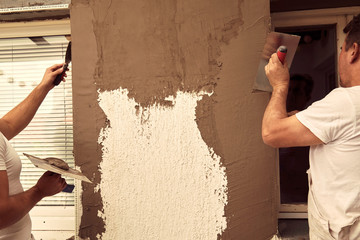 Construction workers plaster a wall.