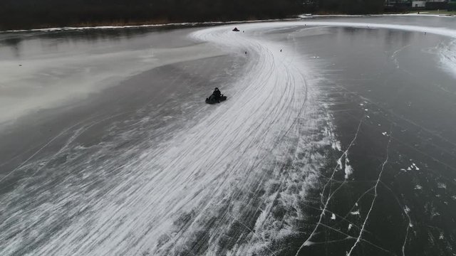 Low altitude aerial view of go-karts also written as go-carts often referred to as simply karts cornering over frozen lake track moving sideways through corners awsome winter sports activity 4k