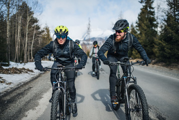 Group of mountain bikers riding on road outdoors in winter.