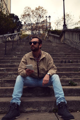 Obraz premium Handsome man sitting on stairs and using cellphone.