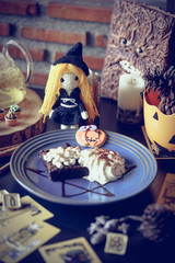 Halloween cafe and witchcraft party with herbal afternoon tea and macaron dessert in wicca and pegan concept with tarot cards. Selective focus on the cute crochet witch doll. Vignette and dark filter.
