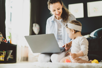 Mother with child sitting on floor watching videos for kids on laptop. Female freelancer working online remotely at home with baby