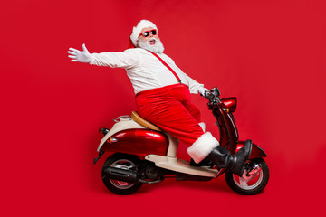 Fototapeta na wymiar Profile side view portrait of nice bearded glad cheerful cheery funny funky Santa riding moped hurry up having fun holly jolly isolated on bright vivid shine vibrant red color background