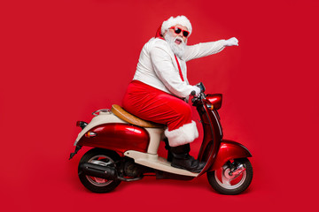 Profile side view portrait of nice bearded cheerful funny funky purposeful Santa Claus riding moped hurry up shopping season North Pole isolated on bright vivid shine vibrant red color background