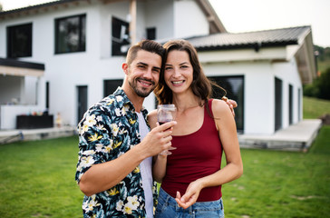 Portrait of young couple with wine outdoors in backyard, looking at camera.