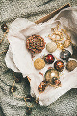 Christmas or New Year preparations. Flat-lay of various vintage Christmas tree decoration toys, balls, garland and pine cones in wooden box over grey knitted background, top view. Festive holiday mood