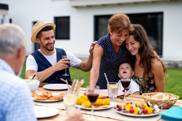 Portrait of multigeneration family sitting at table outdoors on garden barbecue.