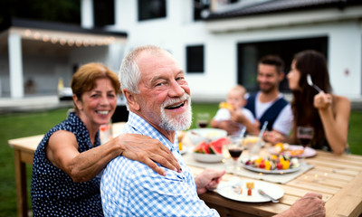 Portrait of multigeneration family sitting at table outdoors on garden barbecue.