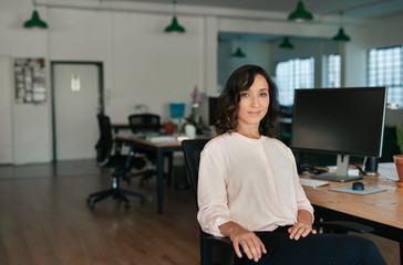 Fototapeta premium Smiling businesswoman sitting at her office desk in the afternoon