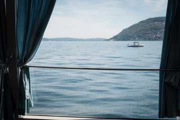 Obraz na płótnie Canvas Un bateau et un lac depuis une fenêtre. Un air de voyage. Regarder par la fenêtre. Le Lac Majeur. Voir un bateau et la mer depuis une fenêtre
