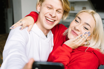 Happy confused blonde couple. Attractive people using mobile phone. Selfie time