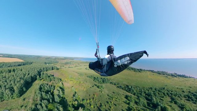 A person is flying the parawing above the green fields