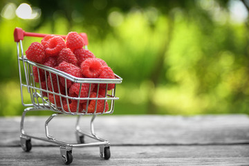  Little metal basket with  raspberry on wooden table in blurred green background. Cart hand
