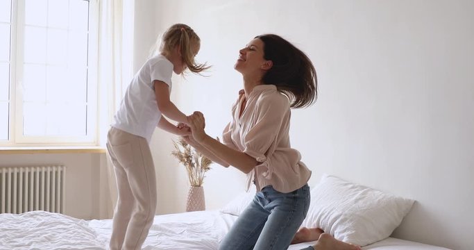Happy mother and child girl holding hands jumping on bed