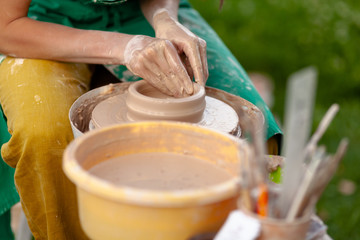 Hand craft making pottery on wheel. Female hands mold ceramic plate from clay (pot).