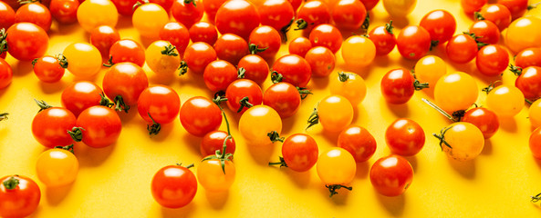 Red and yellow cherry tomatoes on yellow background. Fresh bright organic vegetables.