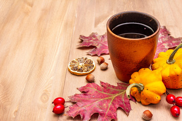 Autumn cozy mood composition. Hot tea in ceramic glass, fall leaves, pumpkins, briar, hazelnuts