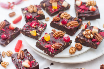 Chocolate fudge with pecan nuts, dried raspberries, strawberries, chewy candies, marshmallow and bites of dark chocolate on white plate and white background.