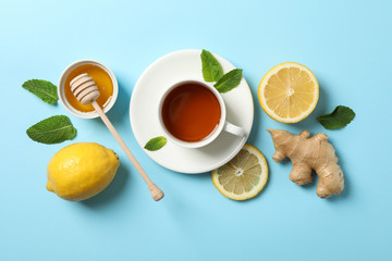Flat lay. Cup of tea, lemon, ginger, mint, honey and dipper on blue background, copy space