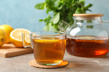 Cup of tea with lemon, teapot and mint on grey background, close up