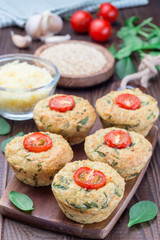 Savory muffins with quinoa, cheese and spinach topped with tomato, on  wooden board, vertical