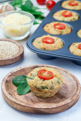Savory muffins with quinoa, cheese and spinach topped with tomato, on wooden plate, vertical