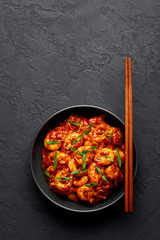 Schezwan Prawns in black bowl at dark slate background. Schezwan Prawns is indo-chinese cuisine curry dish with prawns or shrimps roasted in Schezwan Sauce.