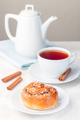 One cinnamon bun on a white plate, served with  cup of red tea, vertical