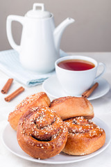 Cinnamon buns on  white plate, served with a cup of red tea, vertical