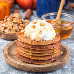 Delicious homemade pumpkin pancakes served with whipping cream, walnuts and honey, autumn decoration, square