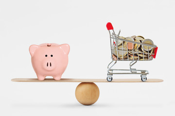 Piggy bank and shopping cart with coins on balance scale