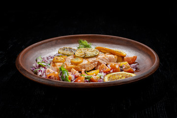 Grilled salmon and vegetables. Laid on a beautiful clay plate, sprinkled with onions, dill and tomatoes.