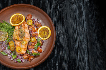 Grilled salmon and vegetables. Laid on a beautiful clay plate, sprinkled with onions, dill and tomatoes.