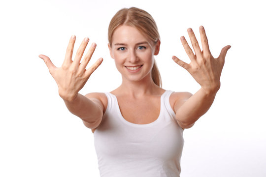 Smiling friendly young woman showing her hands with her fingers splayed towards the camera isolated on white