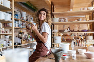 Female potter with smartphone in art studio 