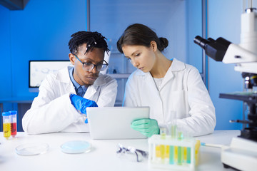 Two young scientists using digital tablet while working on research in laboratory, copy space