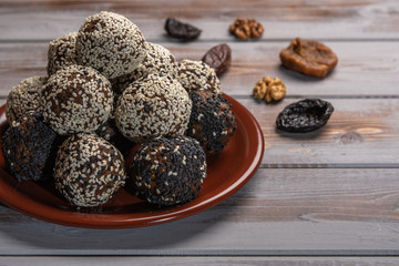 Homemade energy balls on a brown plate on a wooden background. Near the dried fruit