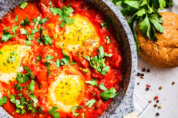 Traditional shakshuka in  pan. Fried eggs in tomato sauce with herbs, top view.