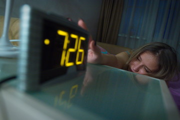 Awakened woman. She reaches out to the clock to turn off the alarm.
