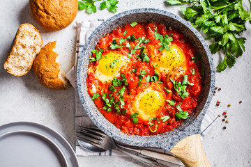 Traditional shakshuka in  pan. Fried eggs in tomato sauce with herbs, top view.