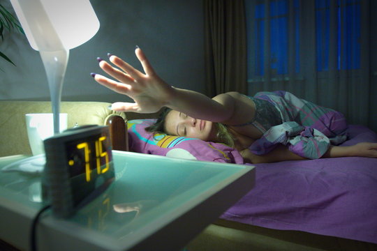 Awakened woman. She reaches out to the clock to turn off the alarm.