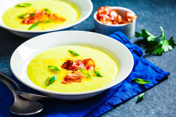 Cheese soup with bacon and green onions in white plate, blue background.