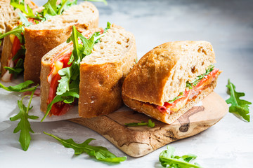 Sandwiches with ciabatta, cheese, ham and vegetables on a wooden board.