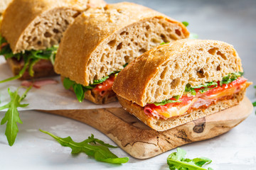 Sandwiches with ciabatta, cheese, ham and vegetables on a wooden board.