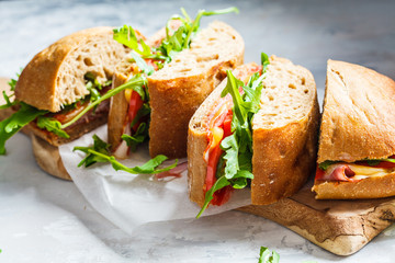 Sandwiches with ciabatta, cheese, ham and vegetables on a wooden board.